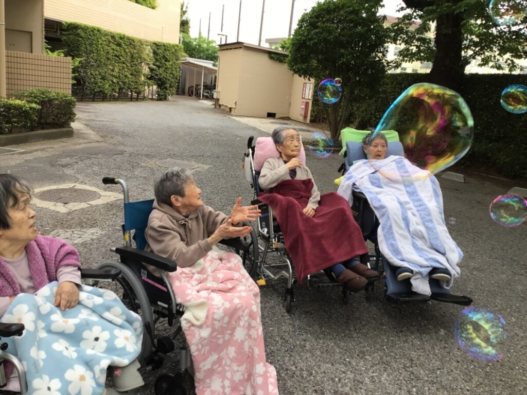 入居者がシャボン玉で遊ぶレクリエーション。中庭での楽しい交流風景。